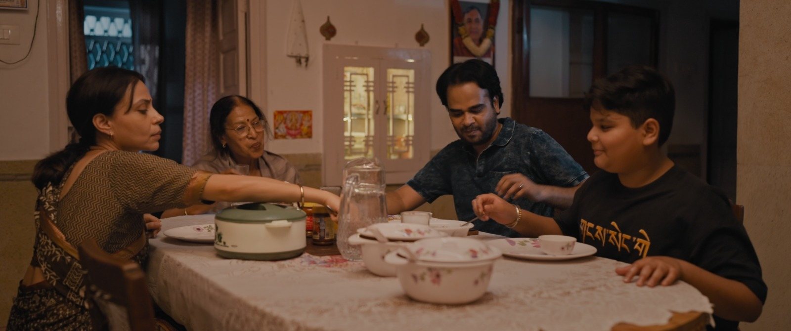 The family gathered around a dining table at a meal, serving dishes between them.