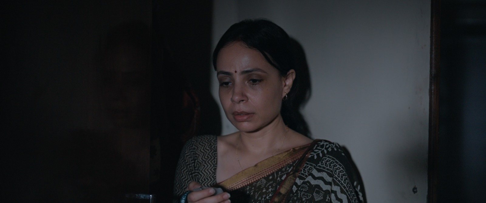 Close portrait of Kavita in a darkened house, looking away from the camera.