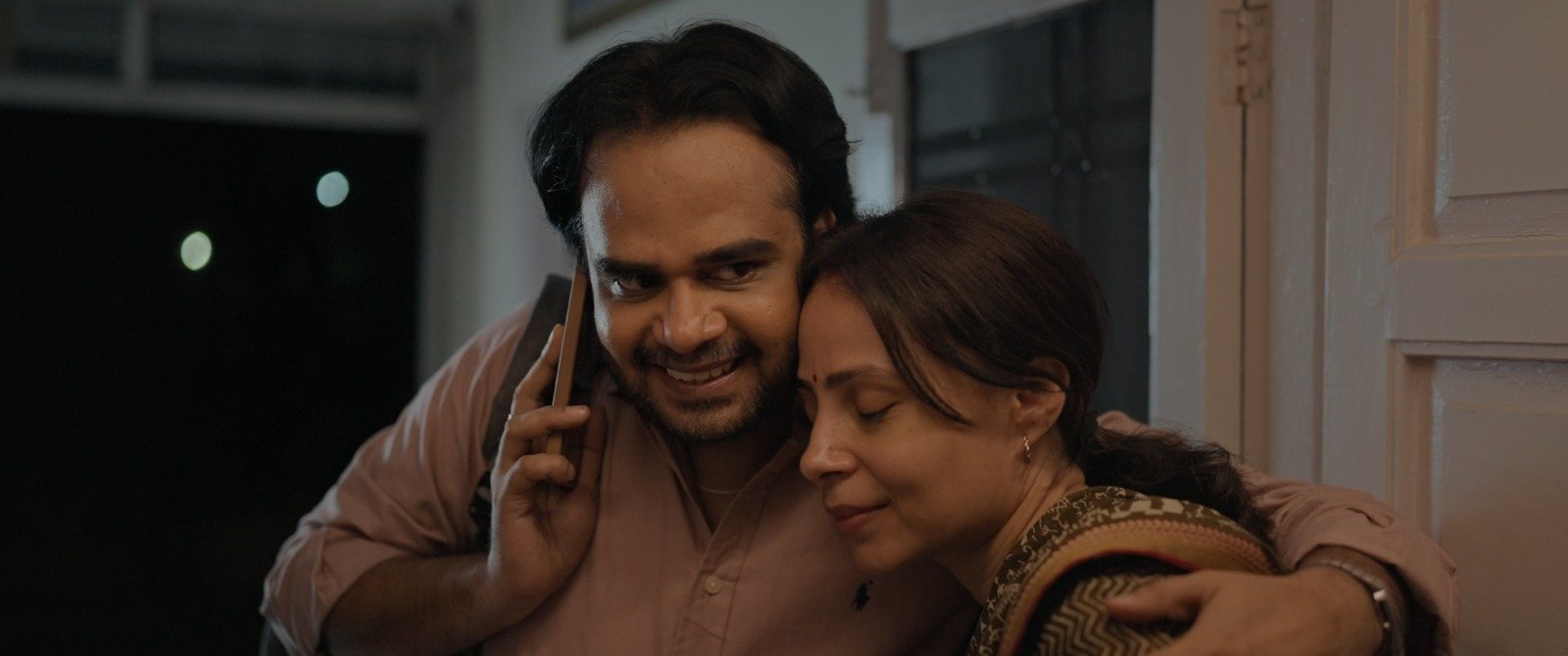 A man on a phone call with Kavita leaning against his shoulder, both smiling.