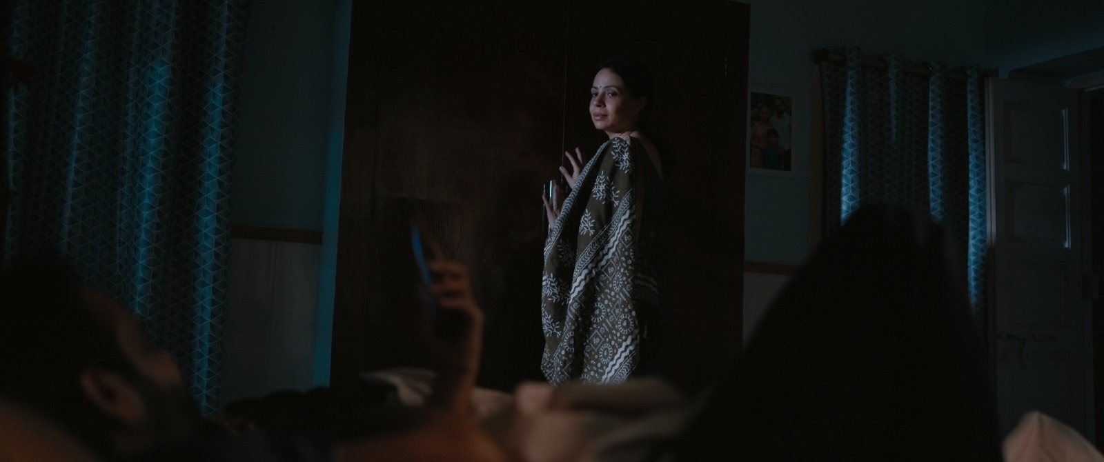 Kavita looking back from a darkened room, framed by a doorway.