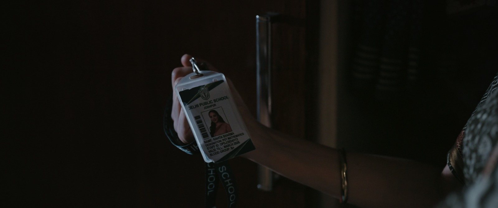 A school identity card held up in a shaft of light in an otherwise dark room.